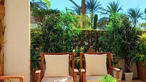 A patio with two wooden chairs and a small table, surrounded by lush greenery and a large tree. - Pool and seaside apartment  (Cannes)