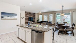 A modern kitchen with a central island, built-in appliances, and a dining area with a wooden table and chairs. - Serene 7-Bedroom Villa in Solterra with Pool (Davenport)