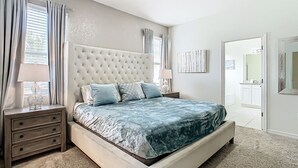 A bedroom with a large bed, a nightstand with drawers, a lamp, and a door leading to another room. - Serene 7-Bedroom Villa in Solterra with Pool (Davenport)