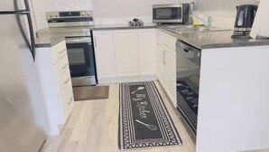 Une cuisine moderne avec des meubles blancs, des appareils en acier inoxydable et un tapis de cuisine noir et blanc.