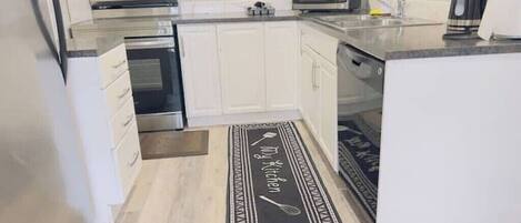 A modern kitchen with white cabinets, stainless steel appliances, and a black and white kitchen mat.