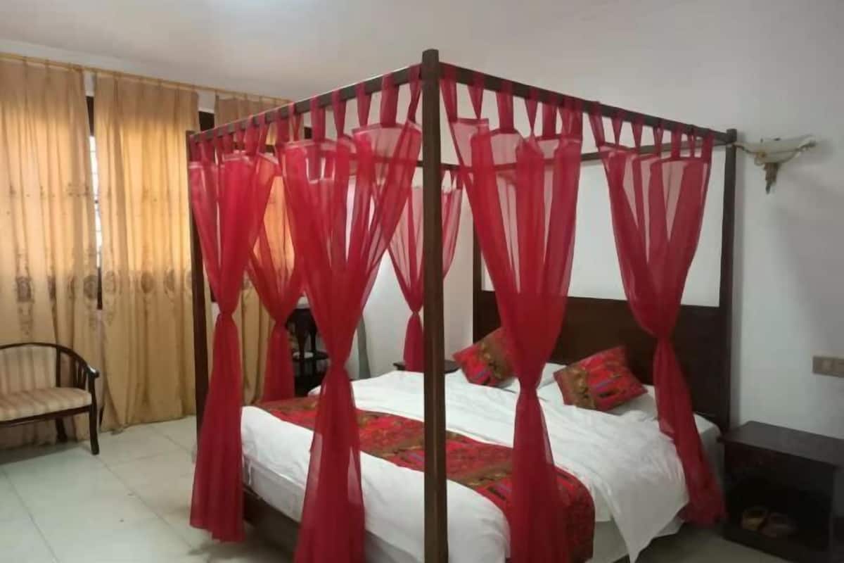 Un lit à baldaquin rouge, une chaise en bois et une petite table de chevet.