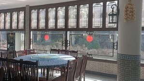 Un comedor con una mesa redonda y sillas, ventanas amplias con cortinas y un pilar decorativo.