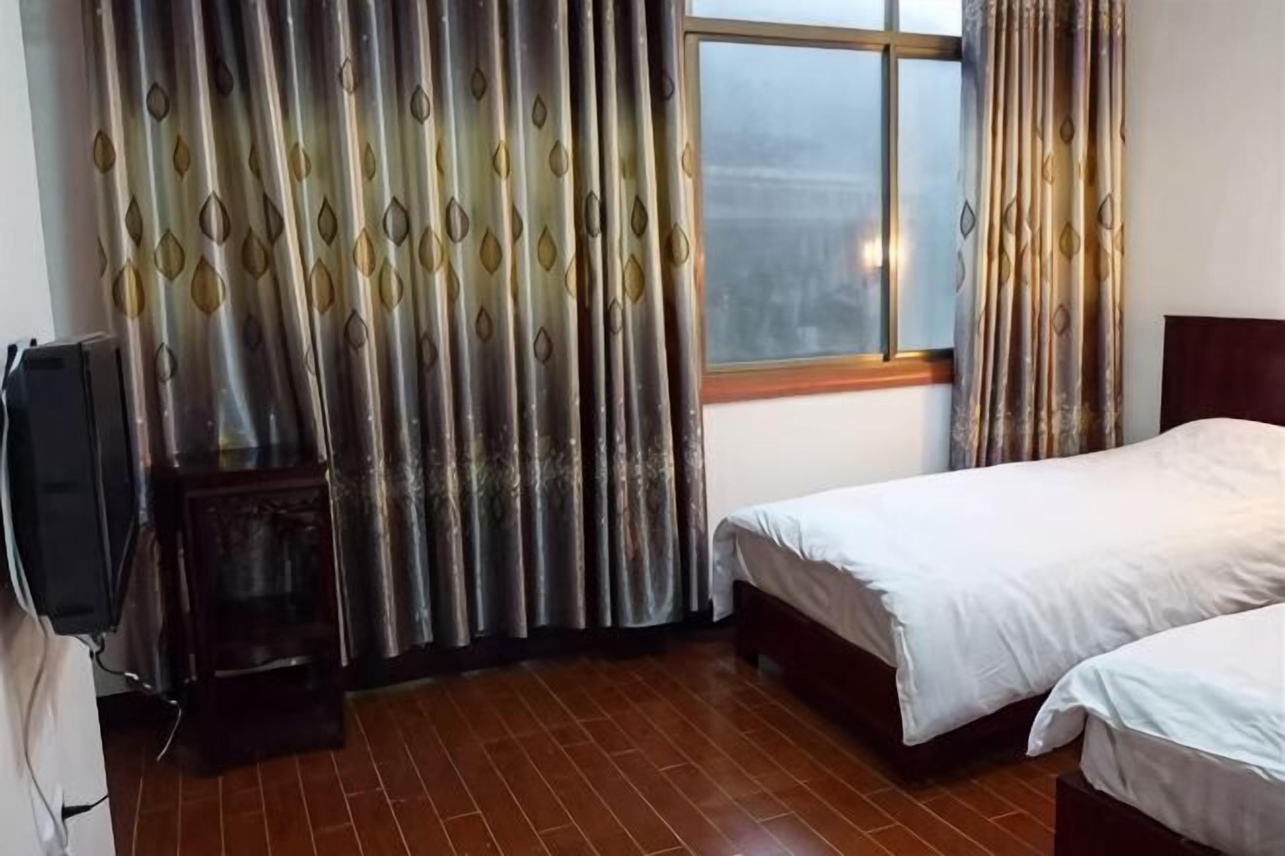 A room with two beds, a window with curtains, a television, and a small cabinet.
