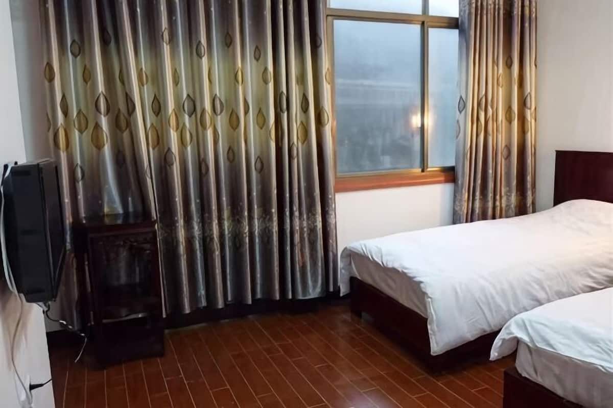 Une chambre avec deux lits, une fenêtre avec des rideaux, une télévision et un petit meuble.