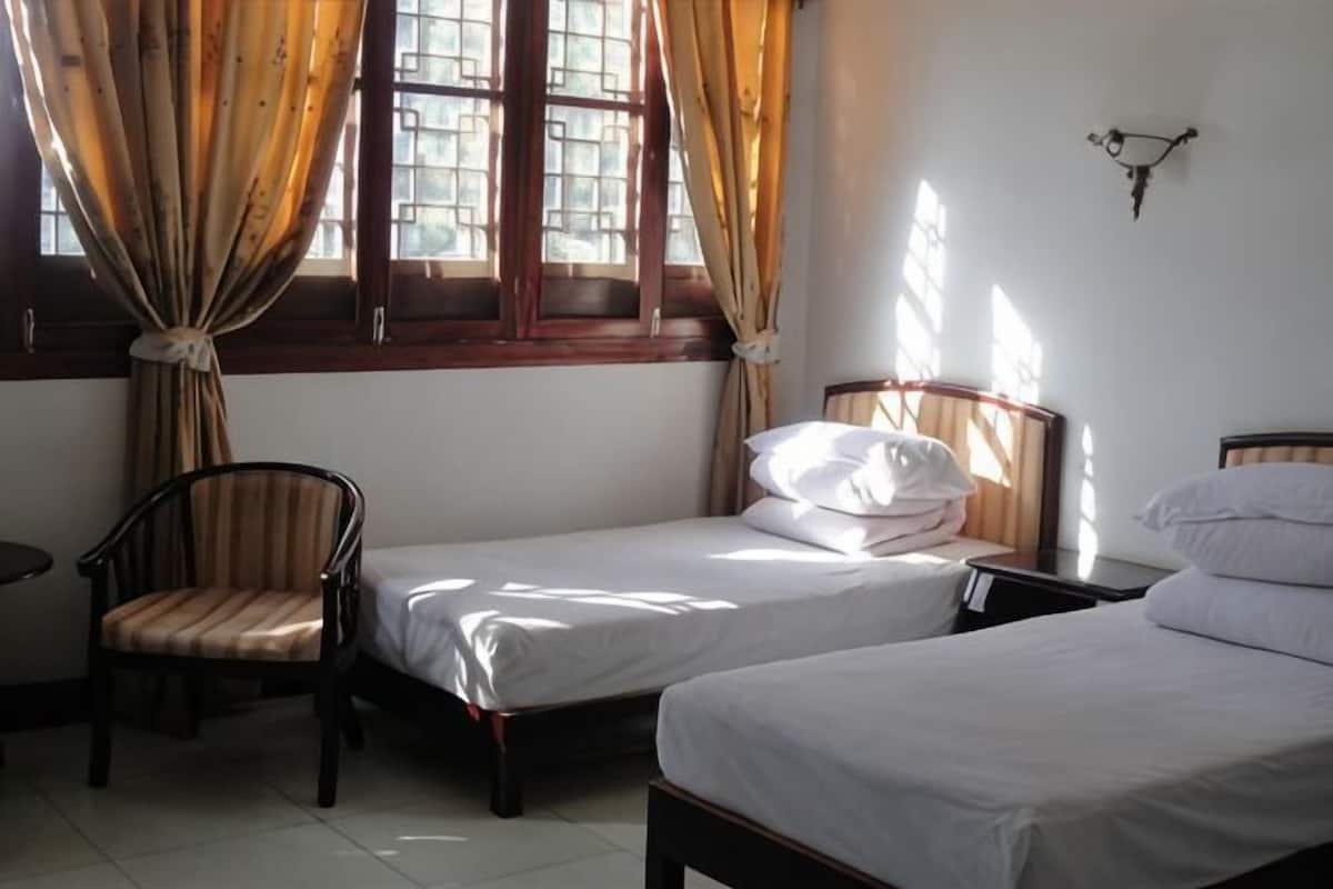 Une chambre avec deux lits simples, une chaise, une table de chevet et une fenêtre avec des rideaux.