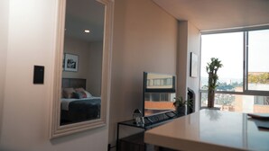 A modern bedroom with a bed, a TV, a small table with a plant, and a window with a city view. - Elegante Apartamento cerca del Tesoro y Provenza by Hoost 2408 (Medellín)
