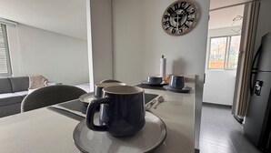 A modern kitchen with a dining table set for two, a decorative wall clock, and a refrigerator. - Elegante Apartamento cerca del Tesoro y Provenza by Hoost 2408 (Medellín)