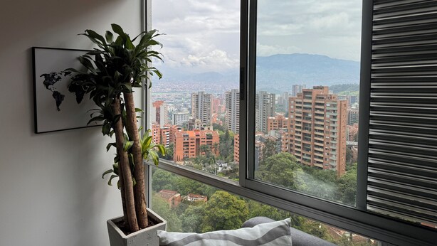 A room with a large window, a potted plant, and a world map on the wall. - Elegante Apartamento cerca del Tesoro y Provenza by Hoost 2408 (Medellín)