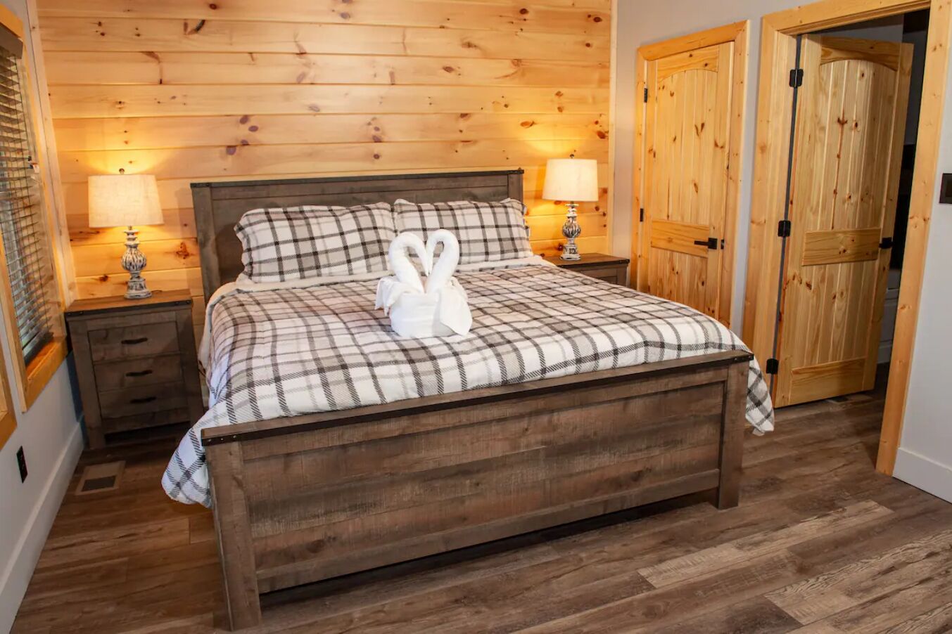 A wooden bed with a plaid bedspread, two bedside lamps, and a pair of swans on the pillows.