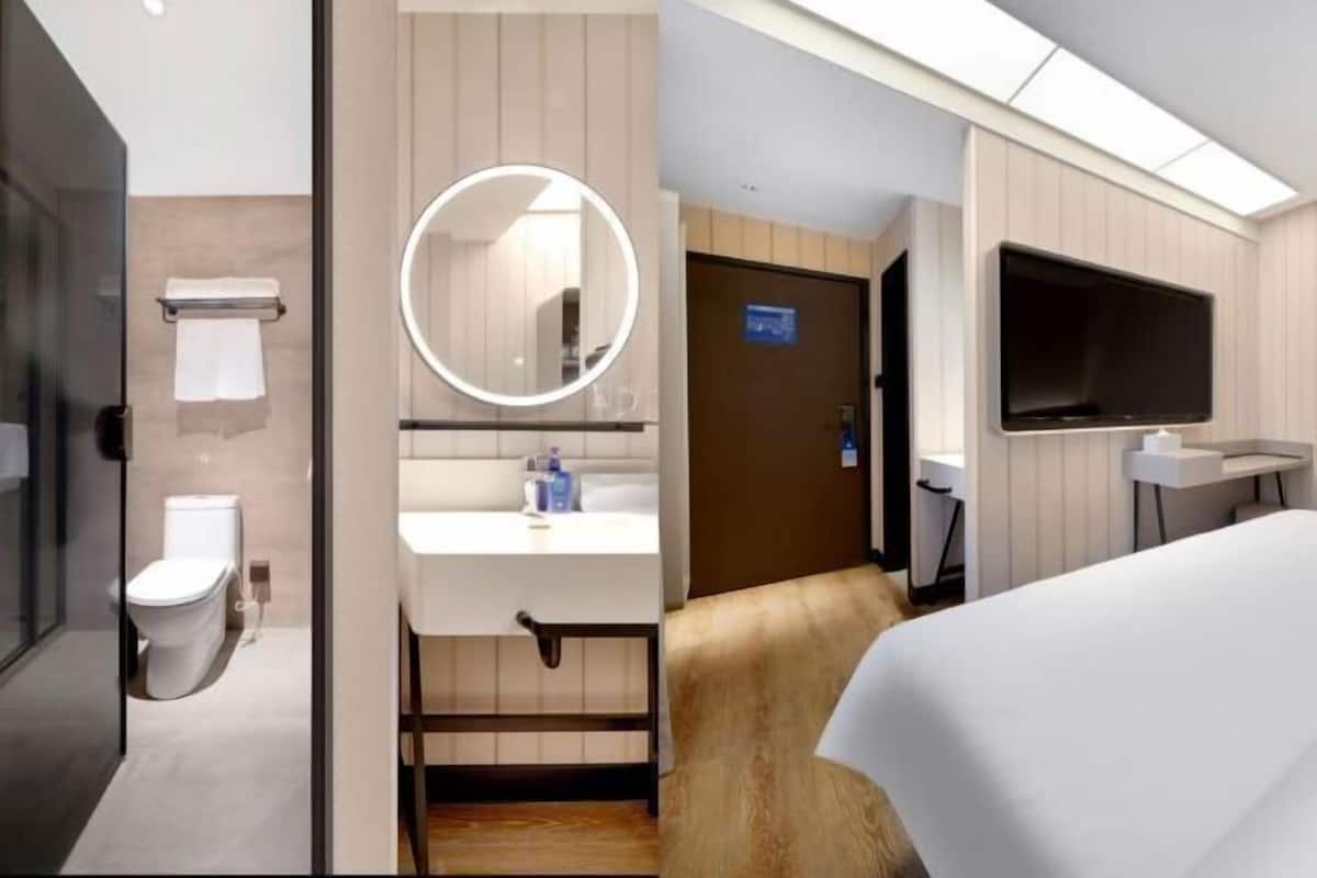 Ein modernes Hotelzimmer mit Toilette, Waschbecken, Spiegel, Fernseher und Bett.