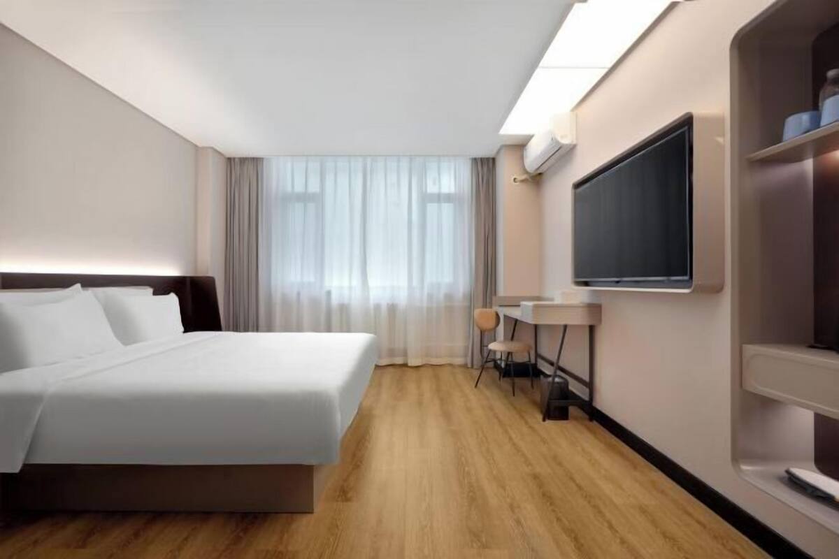 Ein Hotelzimmer mit Bett, Schreibtisch, Sessel, Fernseher und einem Fenster mit Vorhängen.