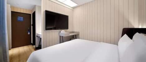 A hotel room with a bed, a TV mounted on the wall, a small bedside table, and a door leading to another room.