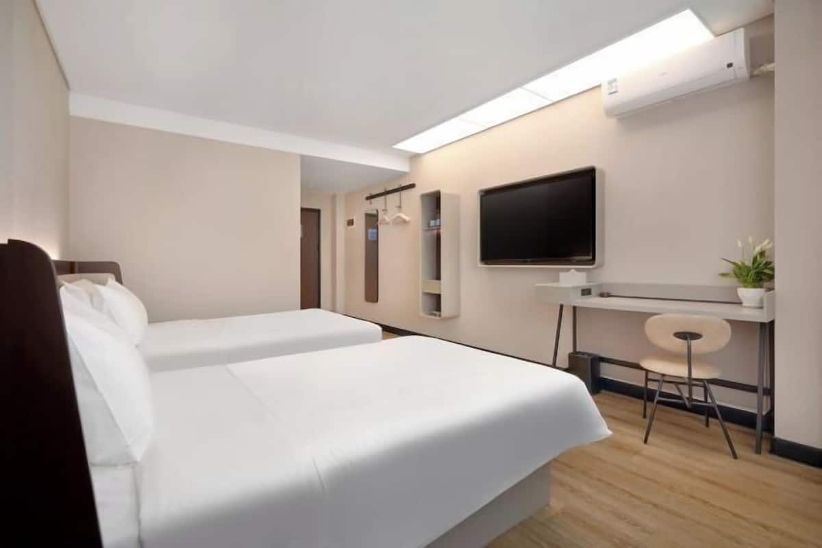Ein Hotelzimmer mit zwei Betten, einem Schreibtisch, einem Stuhl, einem Fernseher und einer Zimmerpflanze.