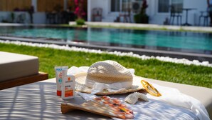 A poolside area with a lounge chair, a sun hat, sunscreen, and a decorative tray with flowers. - Villa Egella (Dikili)