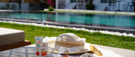 A poolside area with a lounge chair, a sun hat, sunscreen, and a decorative tray with flowers.