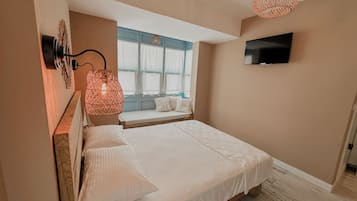 A bedroom with a bed, a TV mounted on the wall, a window with curtains, and a hanging light fixture.
