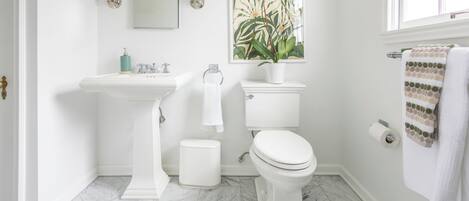 A bathroom with a pedestal sink, toilet, and a large window.