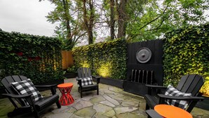Un patio con sillas Adirondack negras, una mesita roja y una parrilla negra.