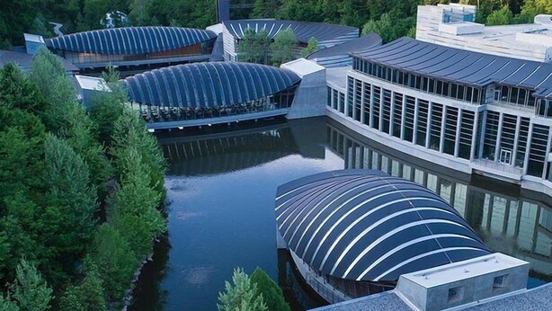 Un edificio moderno con un diseño de techo curvo, rodeado de agua y vegetación.