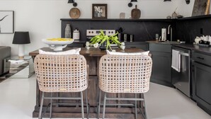 Una cocina moderna con dos taburetes de mimbre, una isla central y una mesa de comedor.