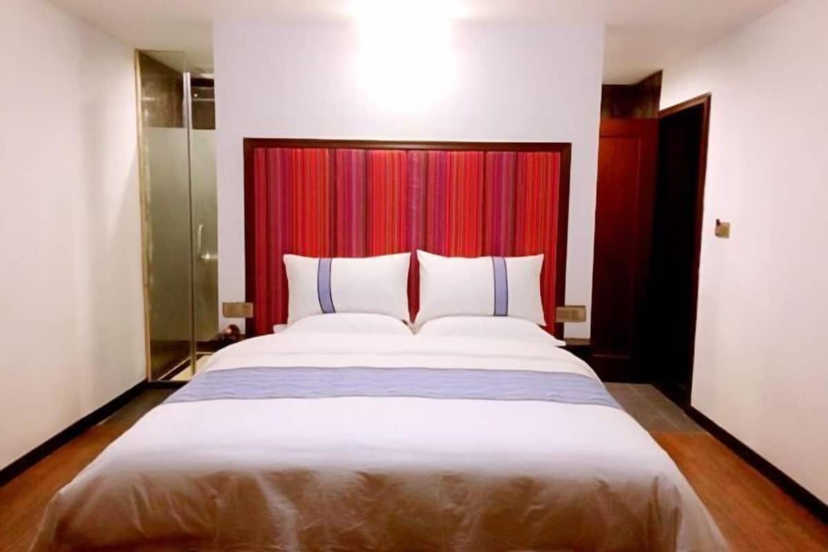 Une chambre d’hôtel avec un grand lit, une tête de lit en tissu rouge et une cabine de douche en verre.