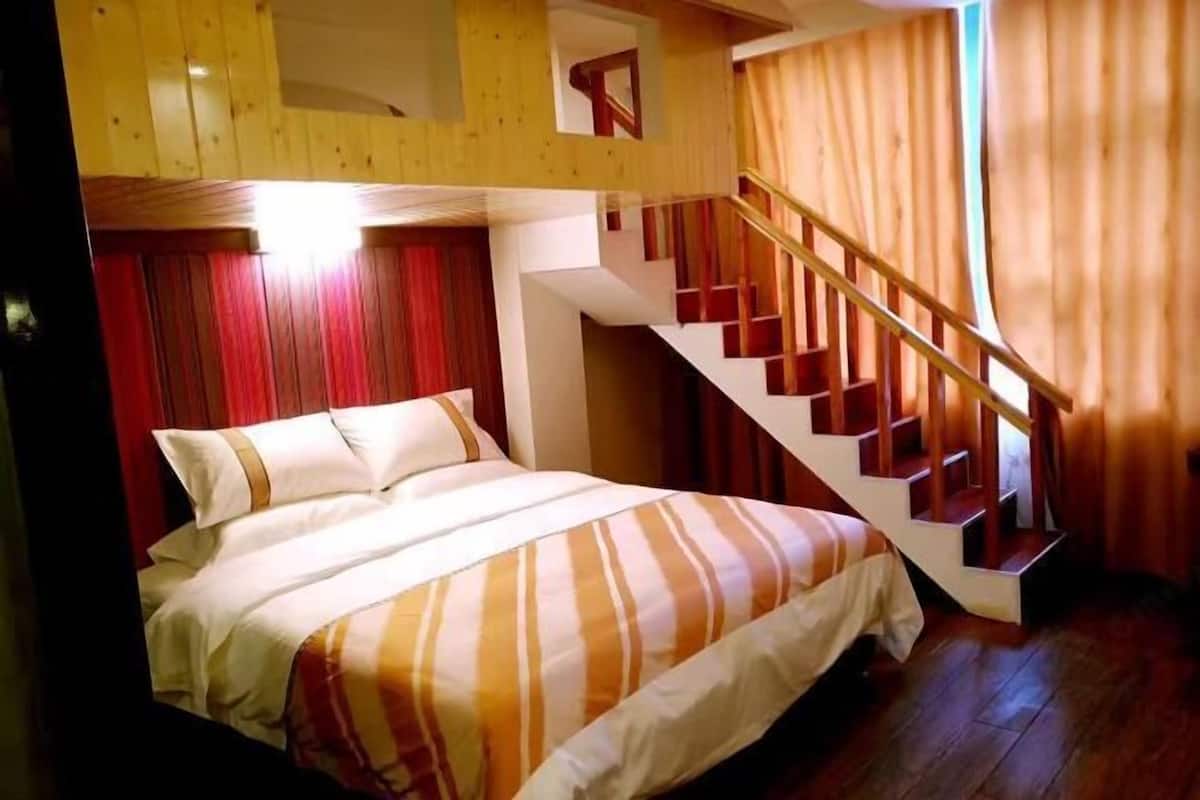 Une chambre à coucher avec un lit, un escalier en bois et un rideau rouge.