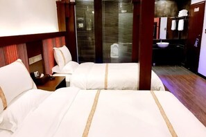 Ein Hotelzimmer mit zwei Betten, Holzboden, einem Badezimmer mit Waschbecken und Spiegel.
