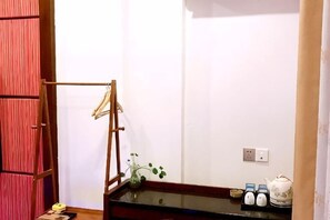 A room with a wooden hanger rack, a small table with a vase and teapots, and a wall socket. - Zhangjiajie Jinhong Homestay (Zhangjiajie)