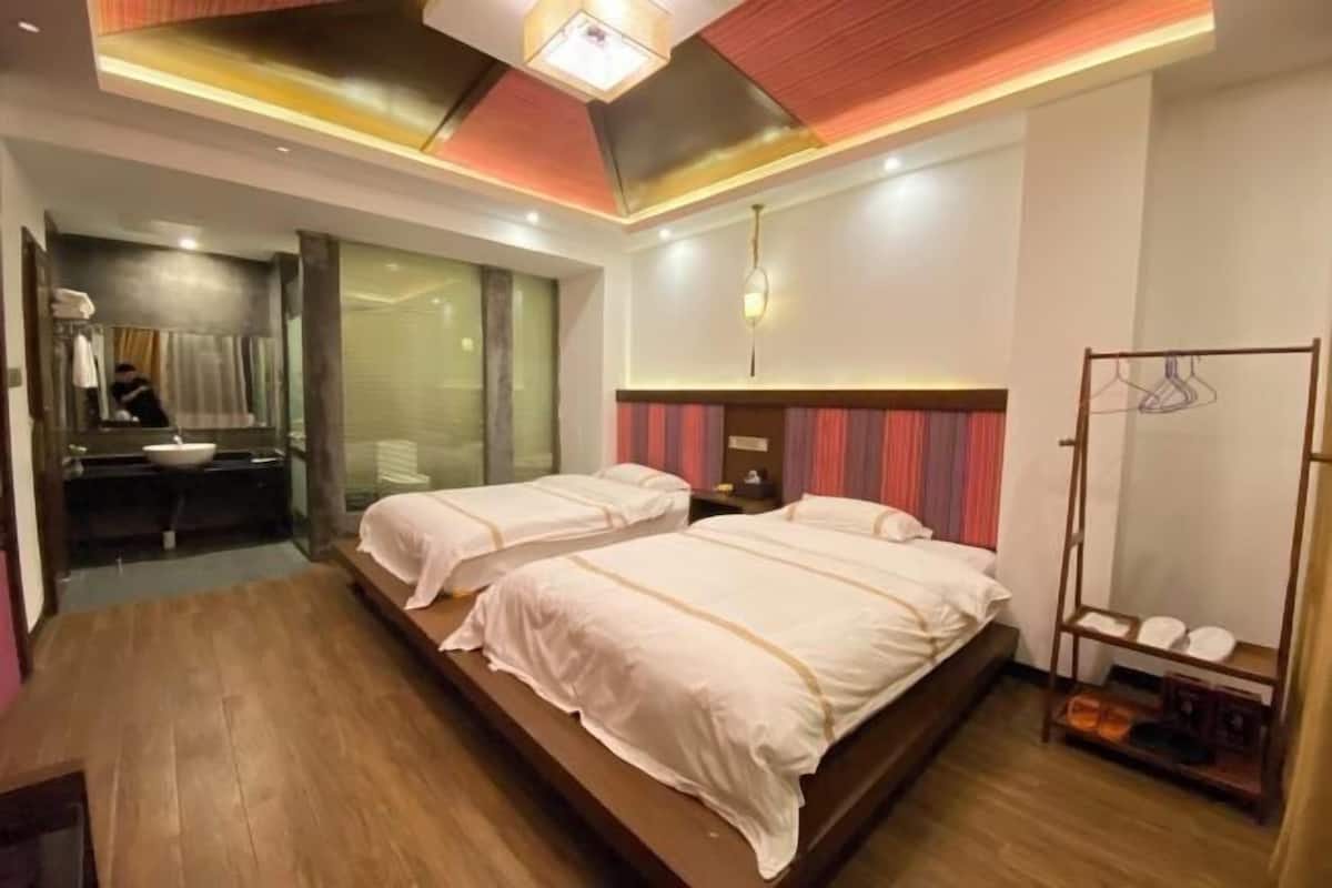 Une chambre d’hôtel avec deux lits, un miroir, une coiffeuse avec un lavabo et un porte-chaussures.