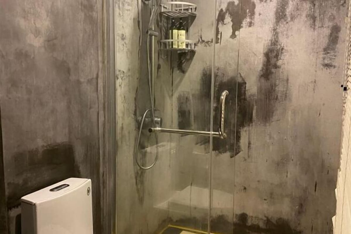 A glass-enclosed shower area with a metal showerhead and a soap dispenser.