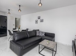 Un salon moderne avec un canapé en cuir noir, une petite table basse et des luminaires suspendus.