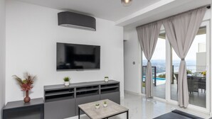 Ein modernes Wohnzimmer mit Flachbildfernseher, grauem Sofa und einem kleinen Tisch mit Pflanzen.