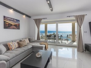 Een moderne woonkamer met een grijze modulaire bank, een zwarte salontafel en een groot raam met uitzicht op zee.