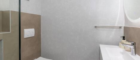 Une salle de bain moderne équipée de toilettes, d’une douche à parois de verre et d’un lavabo avec distributeur de savon.