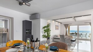 Ein zeitgemäßer Essbereich mit Holztisch, gedeckter Tafel, integriertem Weinkühler und Meerblick durch große Fenster.