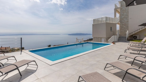 Ein Pool mit Liegestühlen, ein Steinhaus und Meerblick.