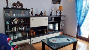 Een woonkamer met een glazen salontafel, een rieten bank en een kast met decoratieve objecten.