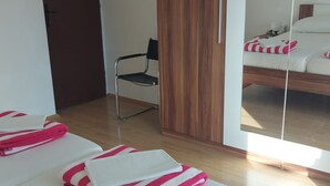 Habitación de hotel con dos camas, un armario de madera, una silla y un espejo grande que refleja la cama.
