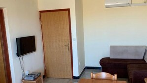 Ein Zimmer mit Holztür, einem an der Wand befestigten Flachbildfernseher, einem braunen Sofa und einem kleinen Tisch.