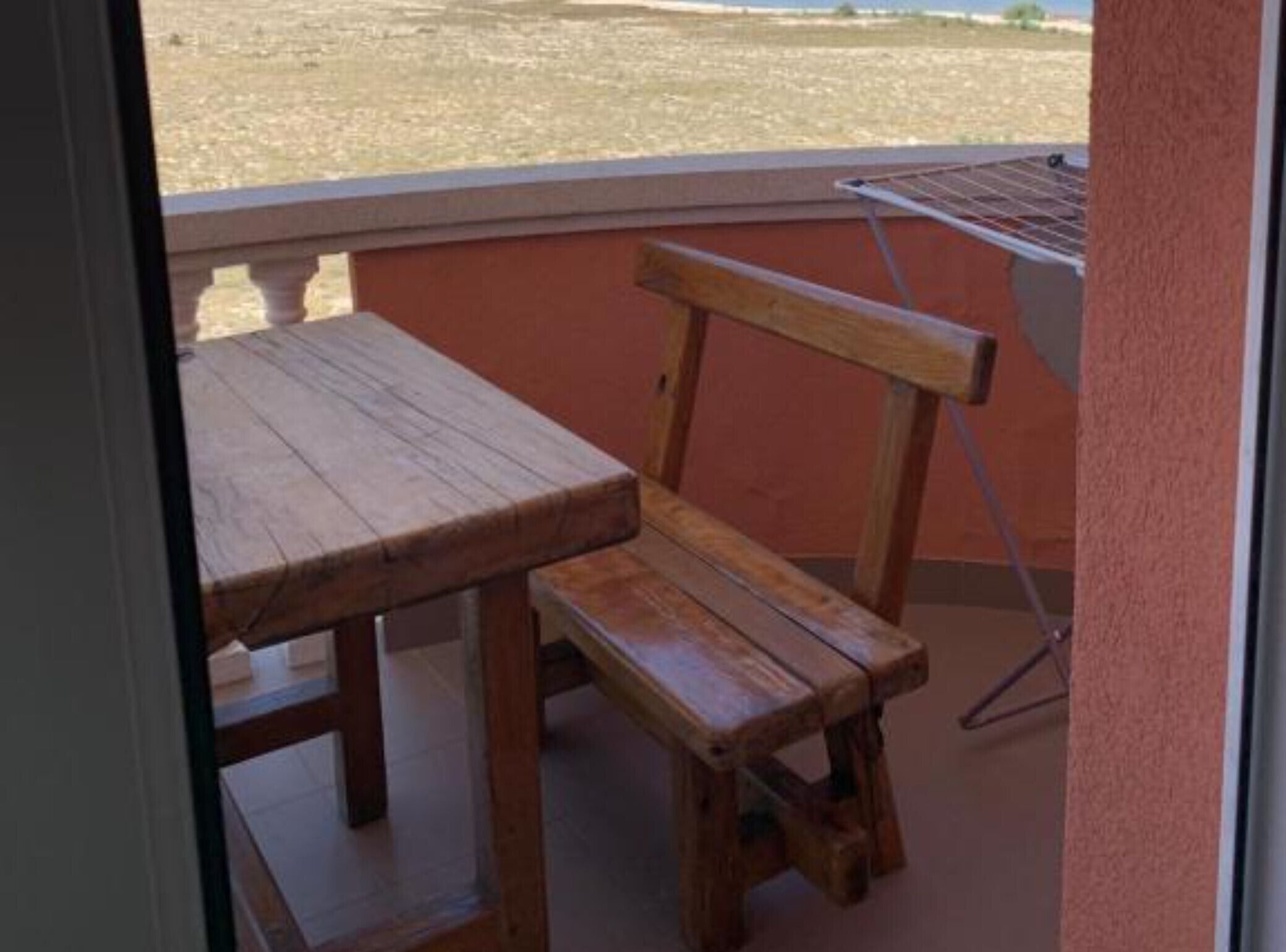 Een houten bank en tafel op een balkon met uitzicht over een droog, open veld.