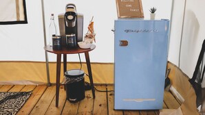 Una habitación con un refrigerador azul, una cafetera y una pequeña mesa con un tazón y una planta.