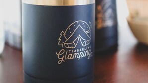 Un vaso azul oscuro con borde dorado y un logotipo que dice 'Timberline Glamping'.