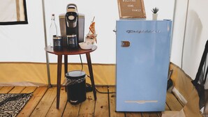 Habitación compacta con un refrigerador azul, una cafetera y una pequeña mesa con un bol y una planta.