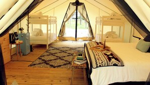 Un hébergement confortable en forme de tente, comprenant deux lits superposés, une petite table avec une lampe et un tapis à motifs sur le sol.