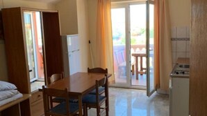 A compact room with a wooden dining table, two chairs, a small kitchenette, and a sliding glass door leading to an outdoor area. - One Bedroom with Balcony and Sea View 2 (Razanac)