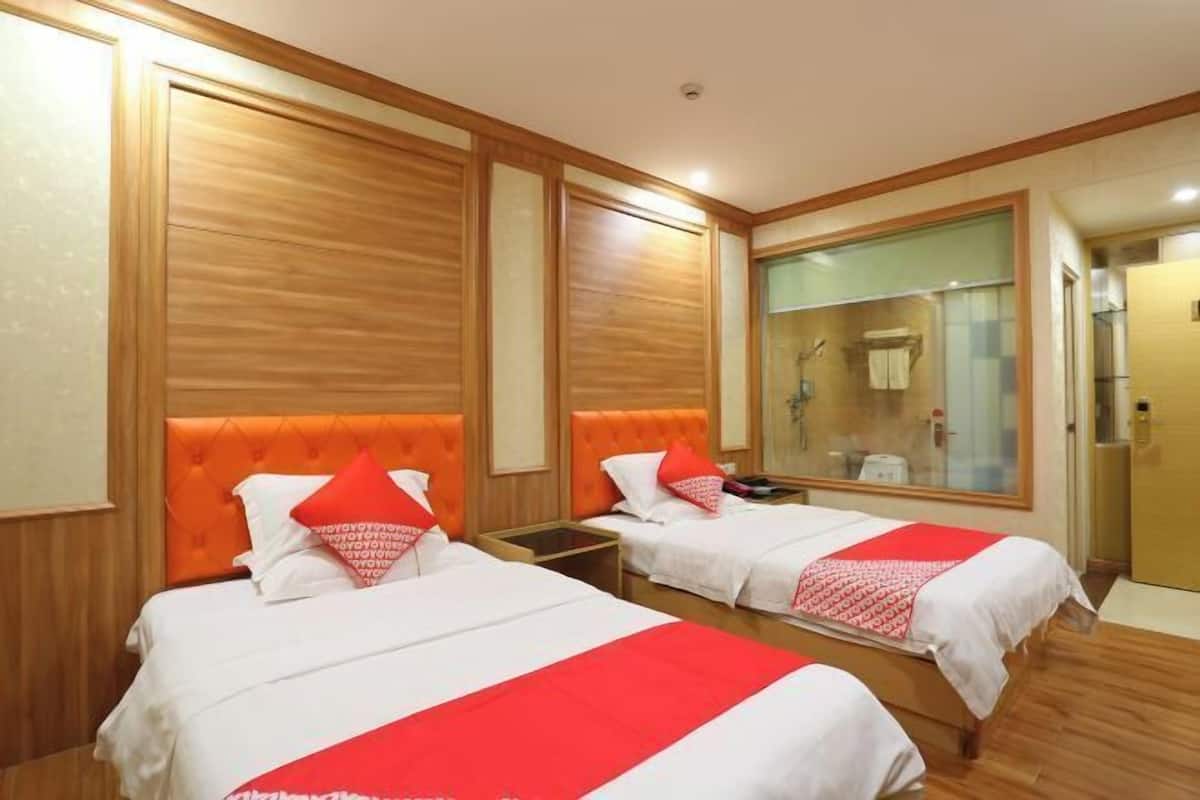 Ein Hotelzimmer mit zwei Betten, Holzvertäfelung, einem großen Spiegel und einem durch eine Glastür einsehbaren Badezimmer.