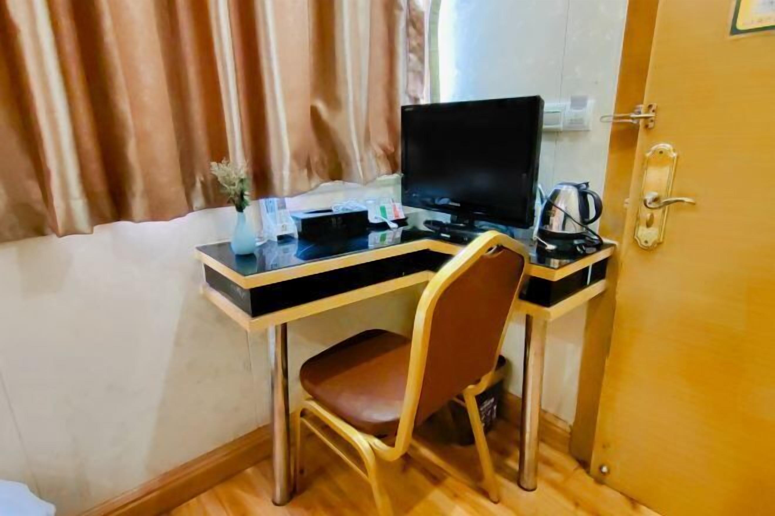 A compact room with a wooden desk, a chair, a television, and a door with a handle.