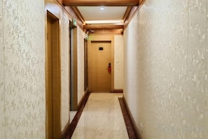 A corridor with a wooden door at the end, a fire extinguisher mounted on the wall, and a textured wall on the left.
