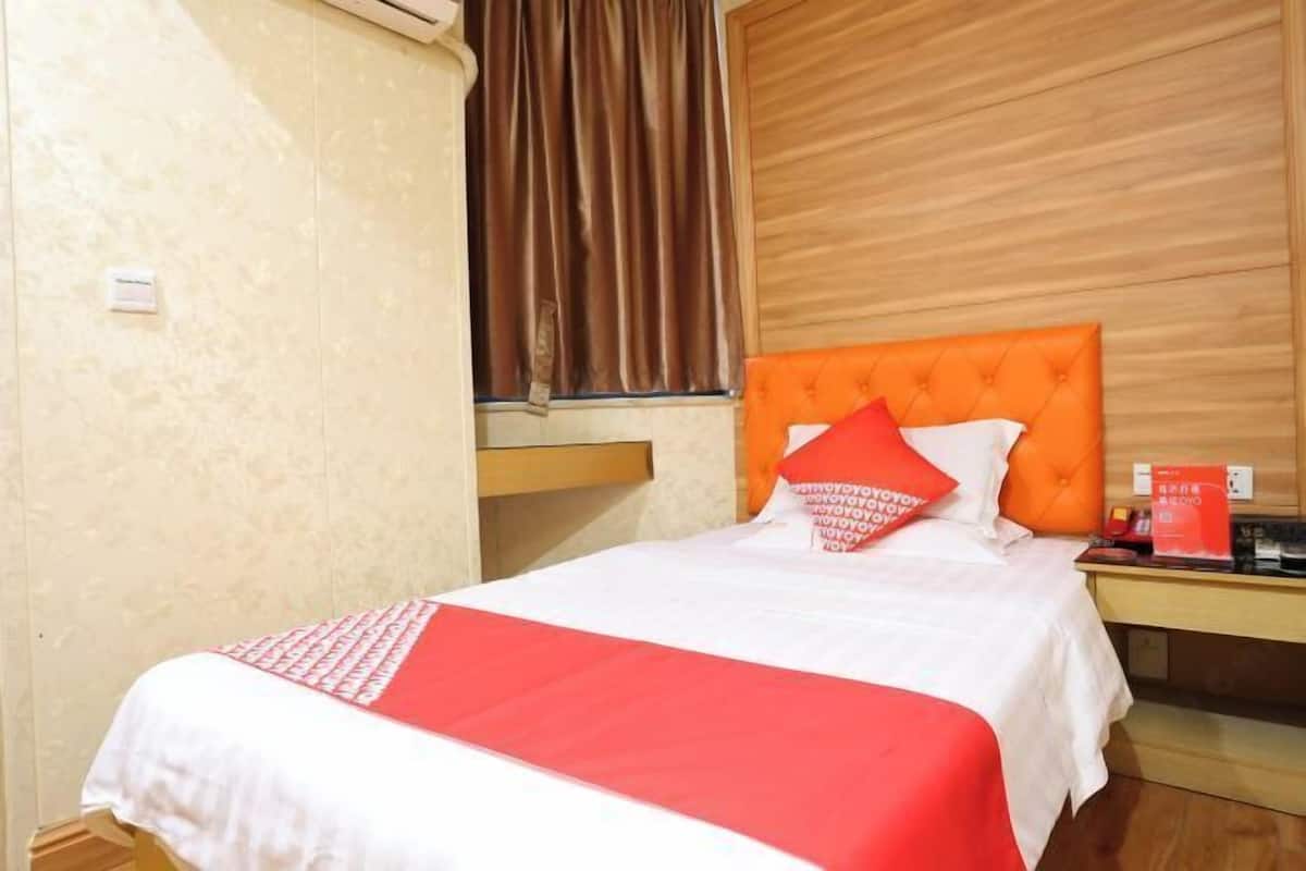Ein Hotelzimmer mit einem Bett, einem Holzkopfstück, einem Nachttisch und einem Fenster mit Vorhängen.